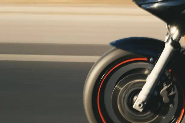 Close up shot of a front tire of a motorcycle going on the road with a motion blur.