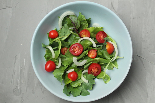 arugula salad of cherry tomato iceberg and sweet onions with a dressing in a setlo blue plate on a gray background with space for text. Healthy delicious food vegetables vitamins.