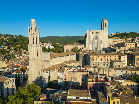 Aerial drone view over the beautiful Catalonian medieval city of Girona, with the famous Basílica de Sant Feliu & Cathedral of Girona dominating the skyline in the heart of the old quarter of the city. Dating back to Roman times, the iconic city is a popular tourist destination in this northern Catalonian region of Spain.