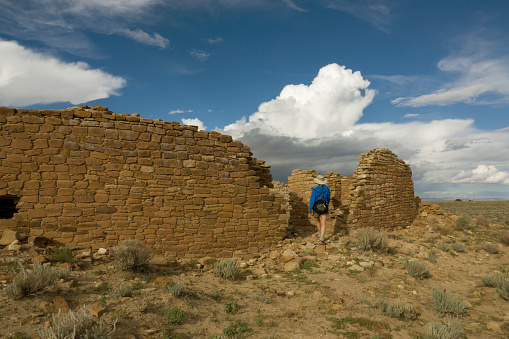 Hiking the South Mesa Trail in Chaco Culture National Historical Park with rain clouds overhead, a woman explores the remaining walls of Tsin Kletsin.