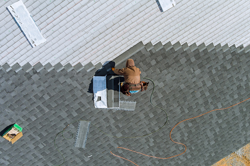 Worker uses an air hammer to nail new shingles bitumen for roof using top view from above