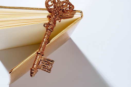 Open book with gold magic key. Wizardry. A shiny glitter gold key lies on the white pages of an open book.