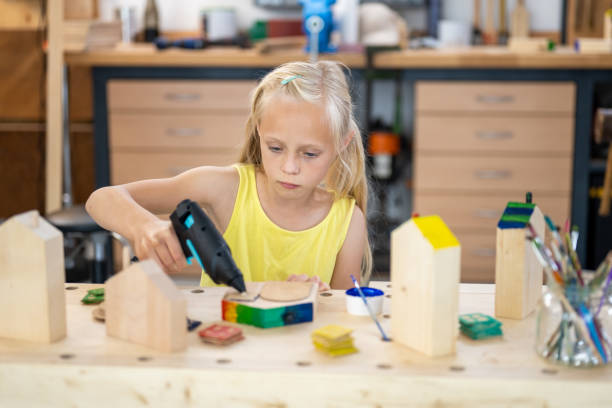 istock Girl using hot glue gun at carpentry art class, front view 1433972535