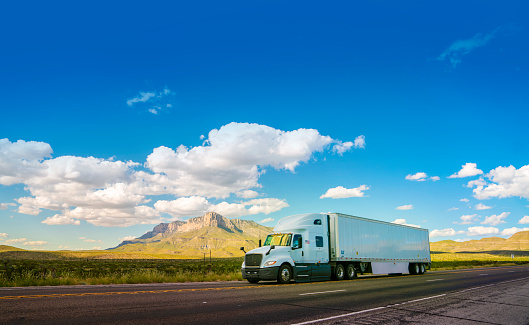 White semi-truck driving on a rural highway in Texas with El Capitan mountain in the back