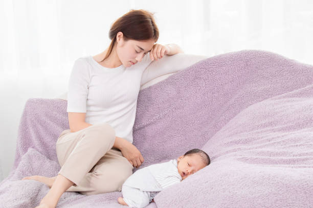 Beautiful Asian mother sitting sleepy next to baby, single mom exhausted from raising children. Newborn sleeping with his head laying in his tiny hands. Beautiful Asian mother sitting sleepy next to baby, single mom exhausted from raising children. Newborn sleeping with his head laying in his tiny hands. asian tired mum stock pictures, royalty-free photos & images