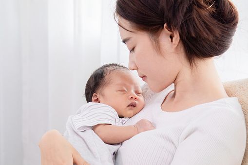Closeup portrait of singlemom asian looking newborn baby while sleeping. Mother holding her newborn in arm with love and care. adorable baby in arm her sleeping with happy and safe.