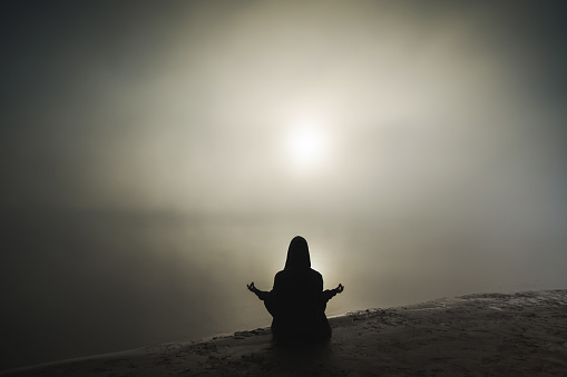 Silhouette of man in meditation on background of foggy dawn.