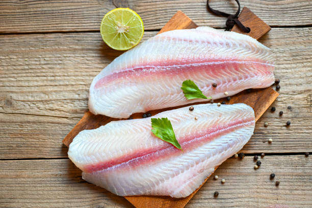 istock Meat dolly fish tilapia striped catfish, fish fillet on wooden board with ingredients for cooking, fresh raw pangasius fish fillet with herb and spices black pepper lemon lime 1434000708