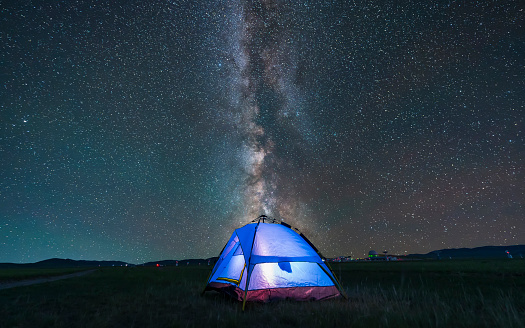 At night, the blue tent is on the grassland. The tent is under the stars