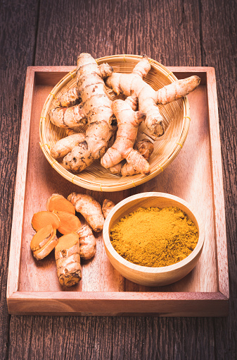 Turmeric Powder and Turmeric root in wooden plate, Curry Powder on a wooden table background.