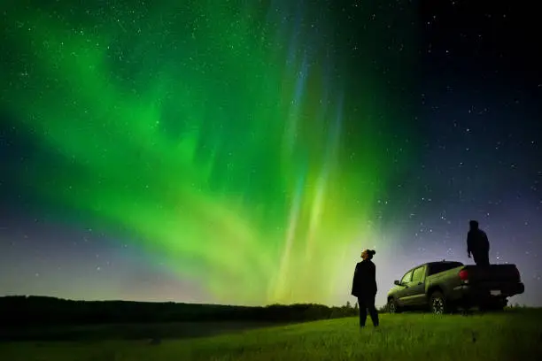 Photo of Couple standing by their pick-up truck watching aurora borealis