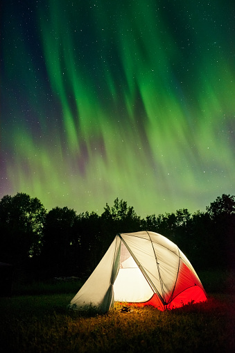 Tent pitched up in field at night with the northern lights flickering in the sky above.
