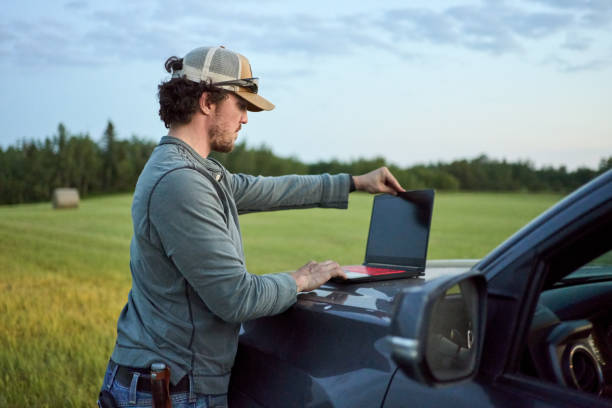 mann, der einen laptop benutzt, während er auf einem bauernhof arbeitet - farmer rural scene laptop computer stock-fotos und bilder