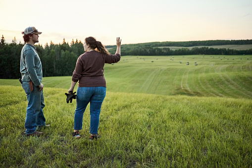 Rear view shot of a male and female farmer standing on a farm field and discussing