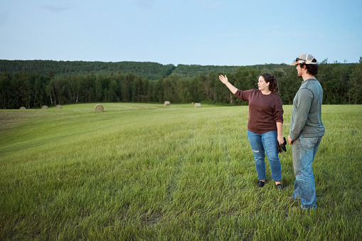 Two young farmers talking while standing together in a crop field