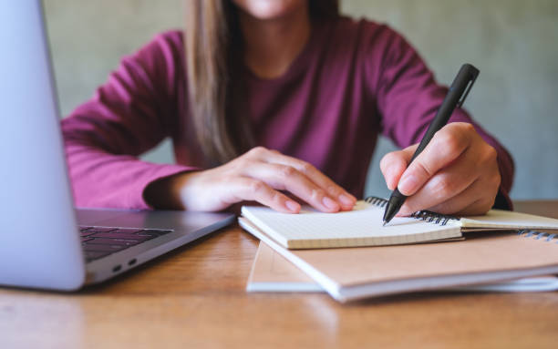 istock Closeup image of a young woman writing on a notebook while working on laptop computer 1434030447