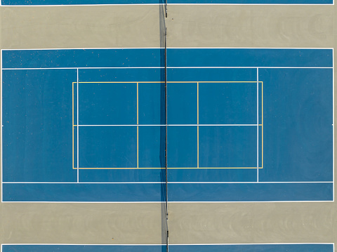 Aerial photo of outdoor blue tennis courts with yellow pickleball lines and gray out of bounds area.