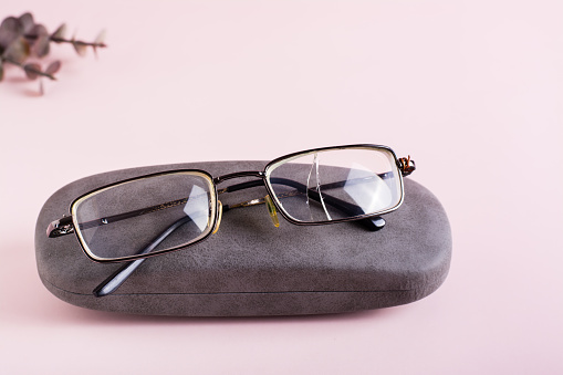 Broken glasses on a hard case on a pink background. The concept of careful storage of optics
