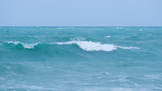 View of sea waves on the beach of tropical seas in Thailand. Strong sea waves crash to shore in the rainy season. Beautiful sea waves with foam of blue and turquoise color.