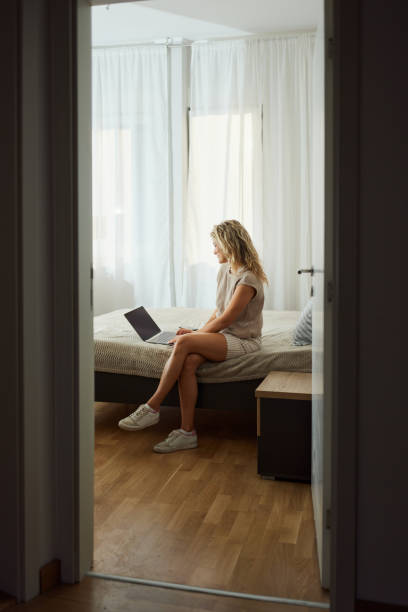 istock Young smiling woman using laptop on a bed in bedroom. 1434049460