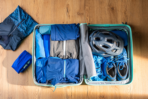 Overhead view of opened luggage with folded clothes, cycling helmet and shoes.