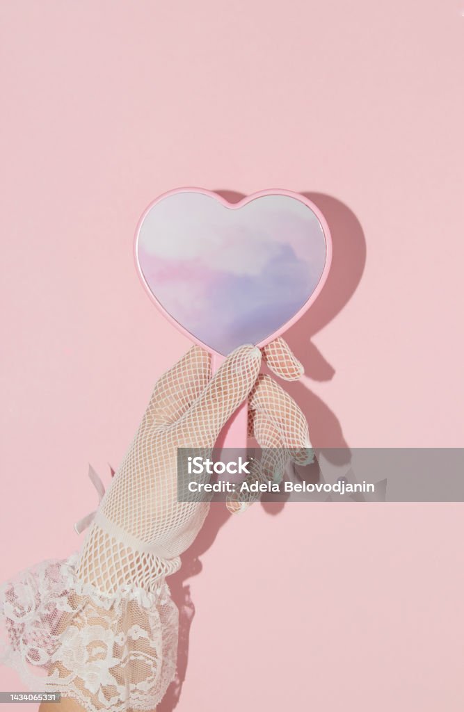 Valentines day creative layout with woman hand holding heart shaped mirror with pink clouds reflection on  pastel baby background. 80s, 90s retro romantic aesthetic love concept. Minimal fashion idea. Mirror - Object Stock Photo