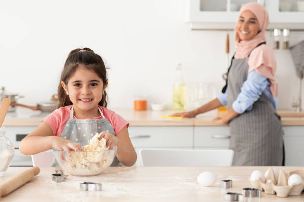 istock Cute Female Child Preparing Dough While Baking With Muslim Mom In Kitchen 1434069735