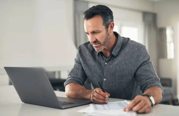 Photo of Mature man, laptop or paper finance for bank loan, trading investment or life insurance savings in house. Thinking remote worker, trader or stock market broker with tech and budget planning documents
