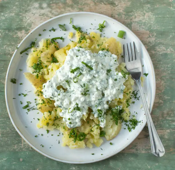 Healthy meal for fitness, diet or healthy eating with boiled and smashed potatoes with peel. Topped with cottage cheese and fresh herbs. Served on a plate isolated on wooden table. Top view