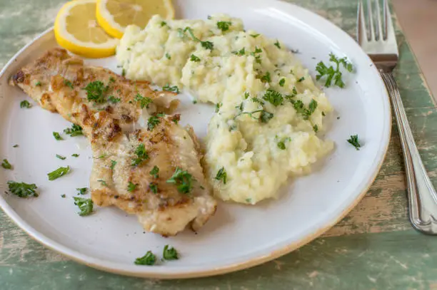 Healthy homemade fresh cooked low carb meal with fish fillet and mashed kohlrabi. Served on a plate with parsley and lemon isolated on wooden table.