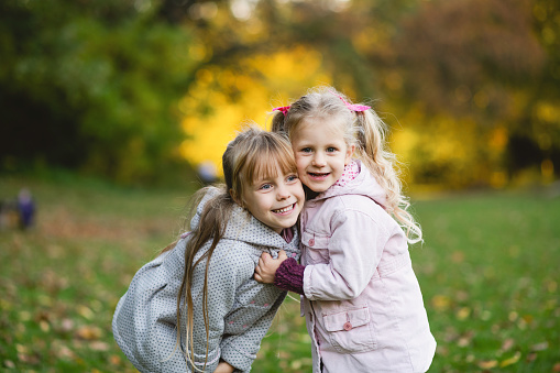 Two child girls play on the lawn in the autumn park. The two sisters are hugging.