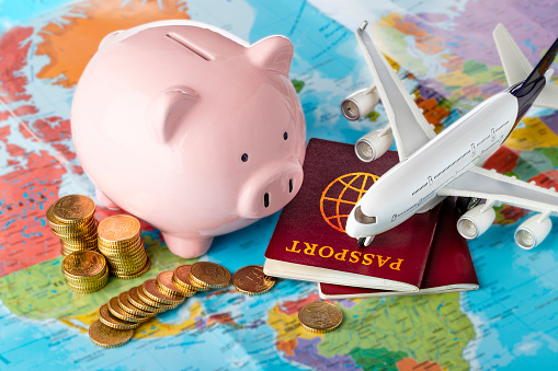 Vacation cost: High angle view of a piggy bank at the top of a world map surrounded by a airplane, two passports and some coins.