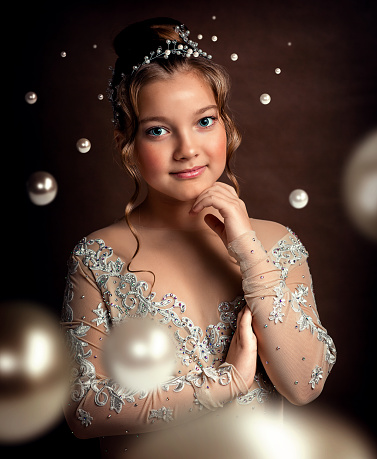 Portrait of a girl of ten years in a white dress. The girl has wavy brown hair and a diadem of pearls on her head. Pearl beads are flying around. She's wearing a bridesmaid dress