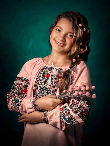 The girl is wearing a pink embroidered shirt, national Ukrainian Slavic clothes, a pink shirt. She holds a bouquet of dried flowers in her hands. Her bouquet consists of craspedia drumstick rosea.