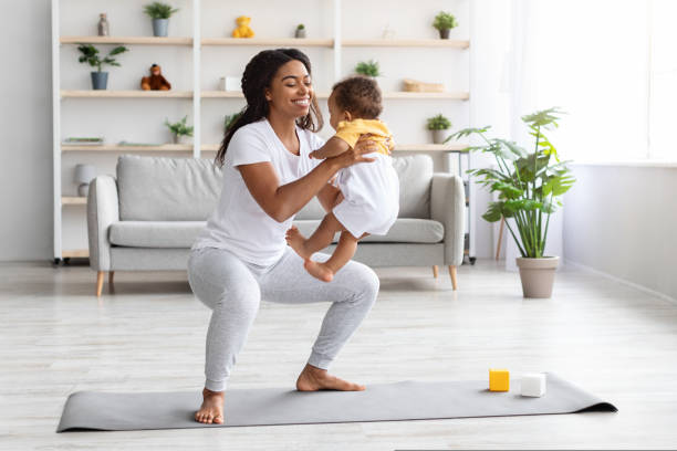 Workout With Baby. Cheerful Black Woman Exercising At Home With Infant Son Workout With Baby. Cheerful Black Woman Exercising At Home With Infant Son, Sporty African American Female Training On Fitness Mat, Holding Her Cute Toddler Child And Making Squats, Copy Space baby squatting stock pictures, royalty-free photos & images