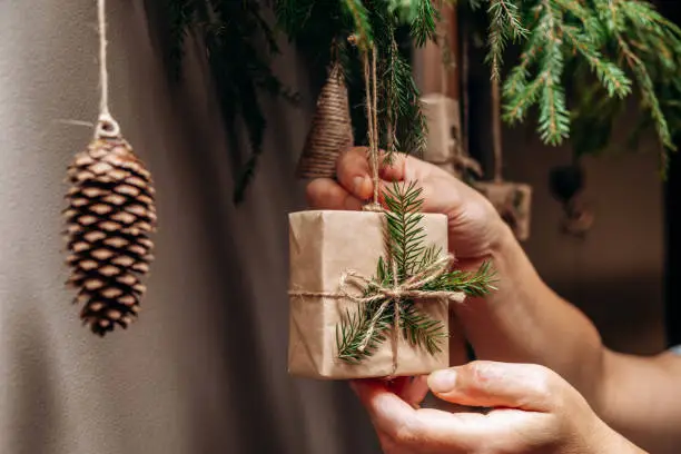 Photo of Christmas decor on the wall.Fir branches decorated with gift boxes in craft paper and fir cones.Eco-friendly concept.New Year and Christmas concept.