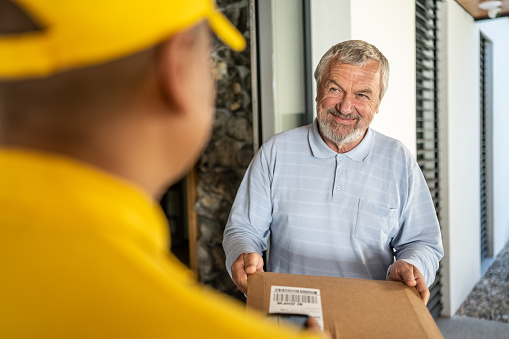 Smiling senior man receiving package from delivery man.