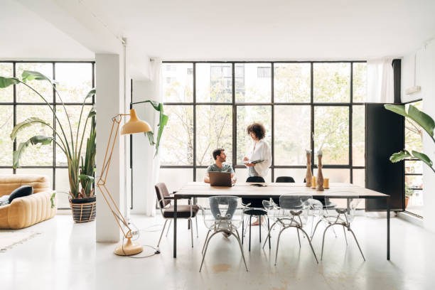 Young multiracial couple working from home. Having conversation. Spacious bright loft apartment. Wearing casual clothes.