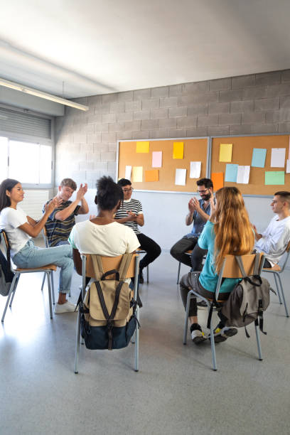 Multiracial group of high school students sitting in a circle clapping together celebrating. Support group.Vertical