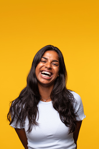 Young Indian woman laughing isolated on yellow background. Studio shot. Vertical image. Happiness concept.