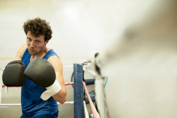 POV photo  of attractive male boxer turned slightly to the side while sparring in the boxing ring; gloved hands raised and with a focused expression and intense look. Copy space, blurred right side, portrait.