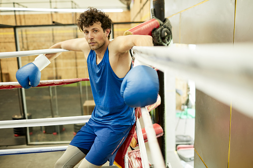 Handsome mid adult male leans back in boxing ring corner to recover after a tough sparring round. Portrait with blurred foreground and background. Copy space