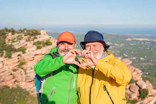 two smiling hiker friends making a heart shape with hands - Healthy lifestyle, self love and active retirement concept