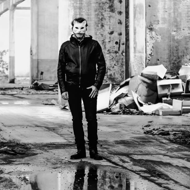 Young man standing in abandoned place while wearing cat mask, black and white