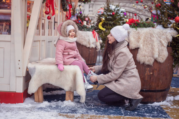 familien-wintersport im park. mama hilft ihrer kleinen tochter, schlittschuhe anzuziehen. weihnachtshintergrund. familien-, weihnachts- und winterurlaubskonzept. - 2 3 months mother child family stock-fotos und bilder