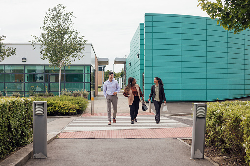 A wide shot of two female and male business people walking into work together. They are all dressed smartly talking and smiling at each other. Based in the North East of England.