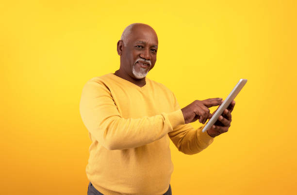 istock Joyful senior African American man using tablet computer for online work or studies on orange studio background 1434104281