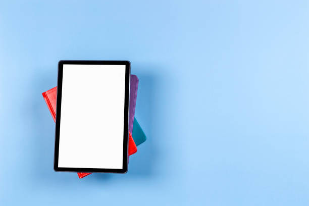 istock Digital tablet computer, e-book reader on top of pile of books on light blue background. Top view, copy space. Mock up 1434105073