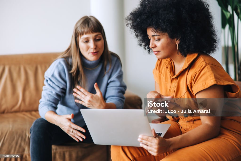 Two businesswomen having a discussion while looking at a laptop screen Two young businesswomen having a discussion while looking at a laptop screen. Two female entrepreneurs working as a team in a modern workplace. Discussion Stock Photo