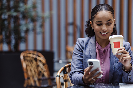 Multiracial young business woman taking a coffee break and using smart phone